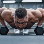 Fit man doing push-ups on hex dumbbells in a modern gym setting.